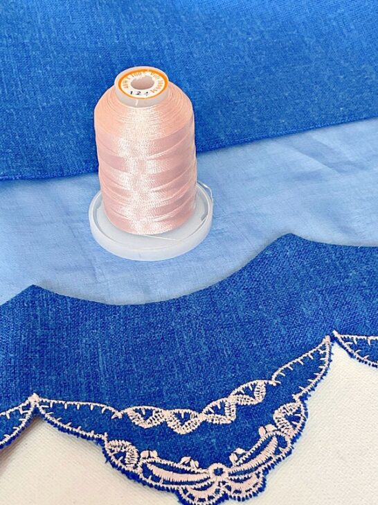 Close-up image of a dress hem adorned with delicate light pink embroidery thread, showcasing intricate stitching and meticulous craftsmanship