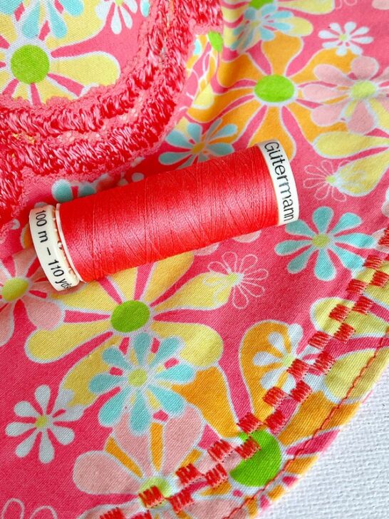 Close-up image featuring decorative stitches made with coral-colored thread on a handmade hat. The stitches create intricate patterns, enhancing the hat's design with vibrant detail and texture.