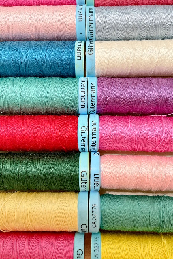 Close-up photograph displaying a range of Gutermann threads in various colors. The threads are neatly arranged on spools