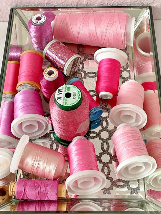 hreads are displayed on spools of different sizes and textures, including silky smooth, durable cotton, and shiny synthetic blends. This image highlights the range of pink tones available for sewing projects