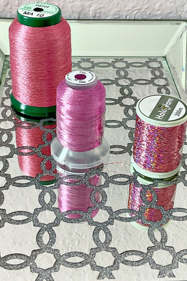 Close-up image of a selection of pink sewing threads, featuring different shades. The threads are neatly wound on spools of various sizes, highlighting their diverse textures.