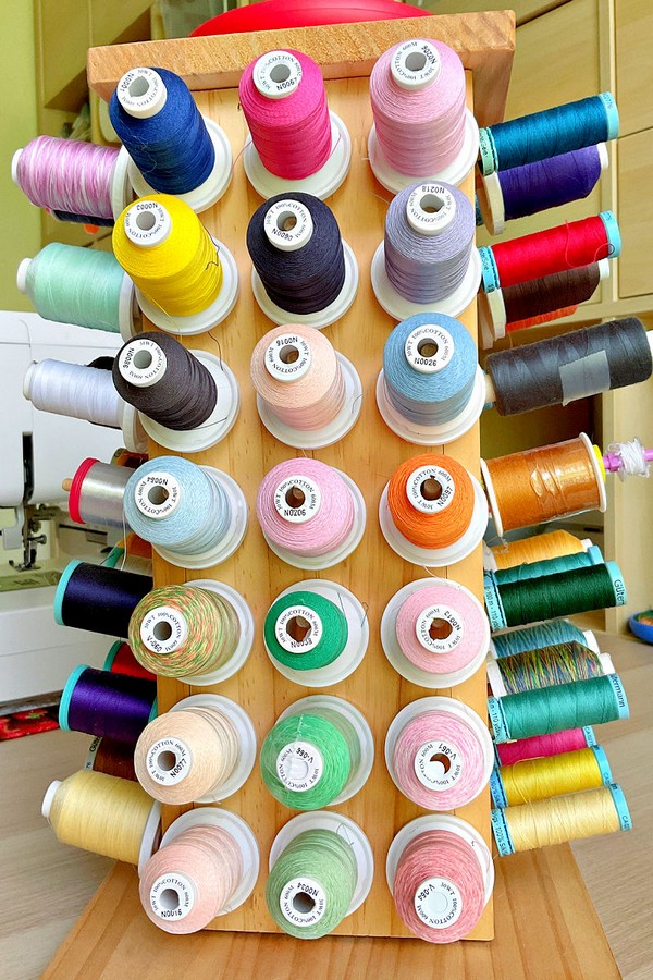 Display of various thread spools arranged neatly on a rack, showcasing a variety of colors and types for sewing and crafting