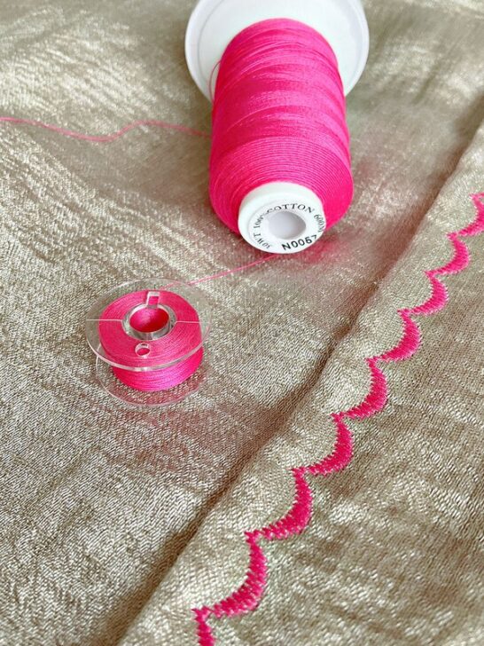 Close-up image of intricate pink thread embroidery on fabric, showcasing detailed stitching and the use of a coordinating bobbin