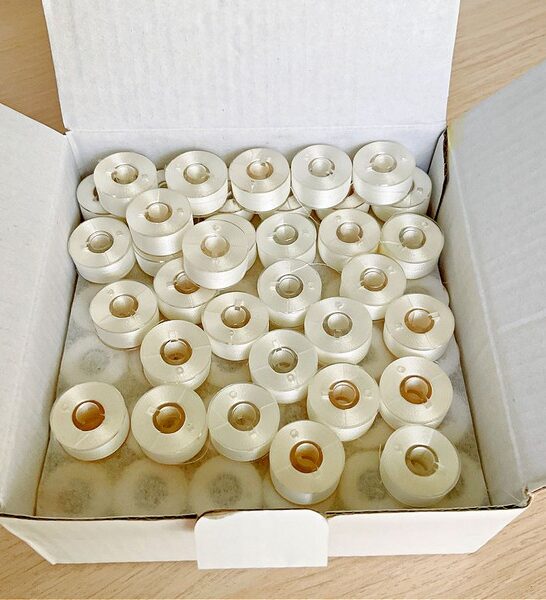 An image of pre-wound bobbins neatly arranged in a box, ready for use in sewing machines