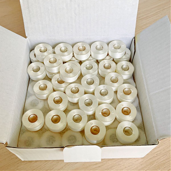 An image of pre-wound bobbins neatly arranged in a box, ready for use in sewing machines