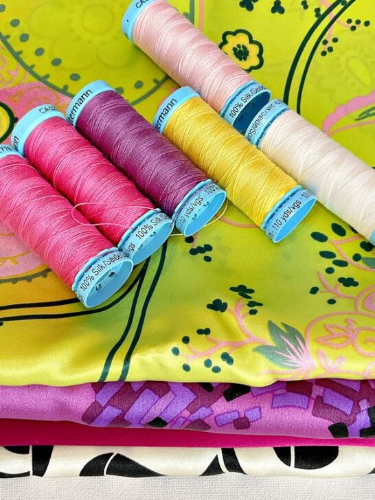 Display of Gutermann silk thread spools in assorted colors, accompanied by vibrant silk fabric