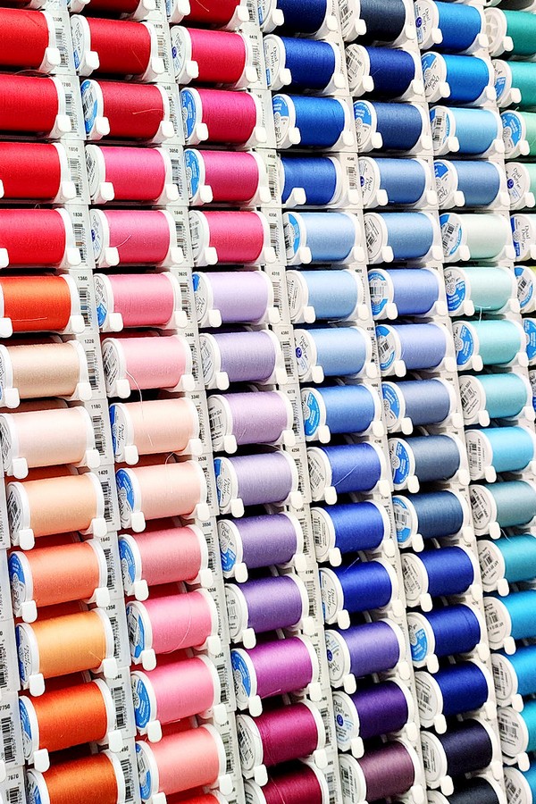 The spools feature an array of colors and textures, neatly organized on the rack, highlighting the diverse selection available for sewing and crafting projects