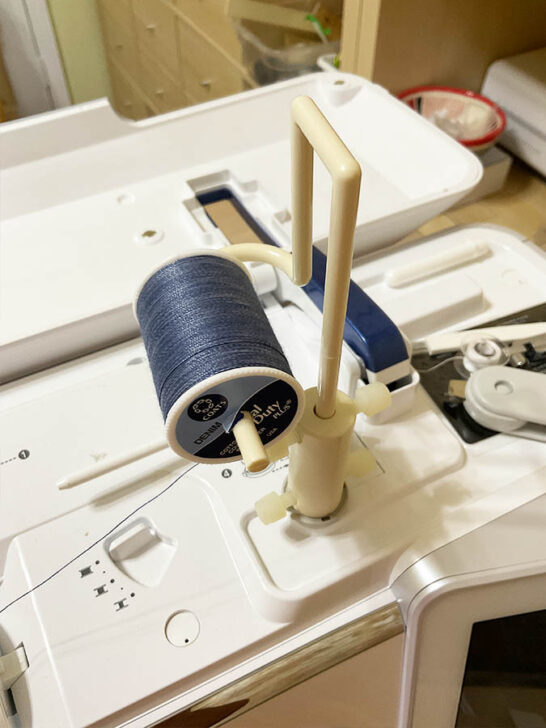 sewing machine featuring a blue thread on its top using a spool pin adapter