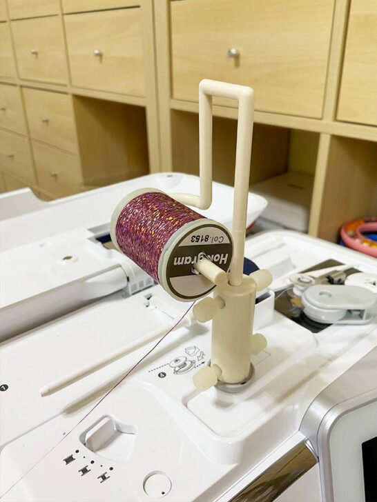 sewing machine featuring a vibrant metallic thread on its top using a spool pin adapter