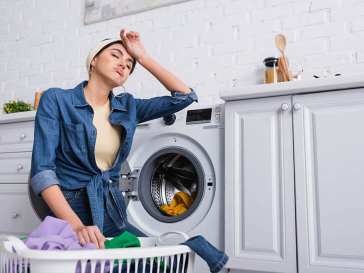 woman with a sad expression sits by a washing machine
