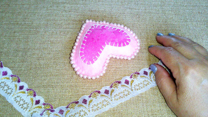 A hand reaches towards a pink heart-shaped cushion with pearl edges