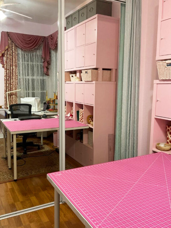 A table with pink mat featuring a sewing machine, surrounded by sewing supplies in a cozy sewing room setting.