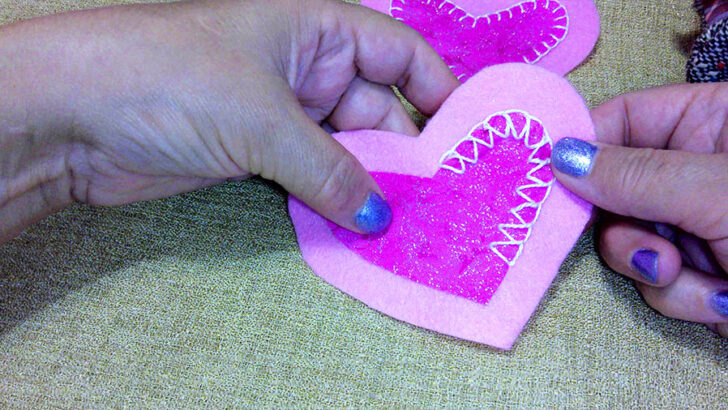 Hands hold a pink felt heart with stitched patterns