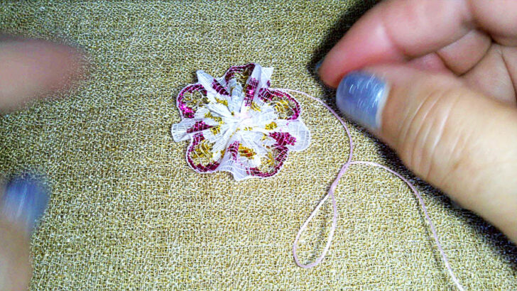 hands sew a delicate pink and white lace flower on textured fabric