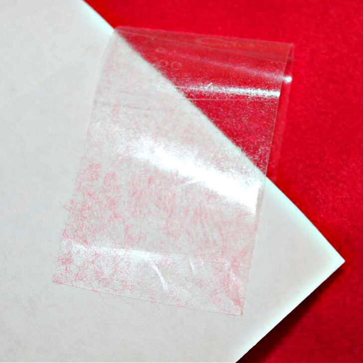 A piece of clear tape used to remove lint, shown on a white paper surface with red lint collected on it.