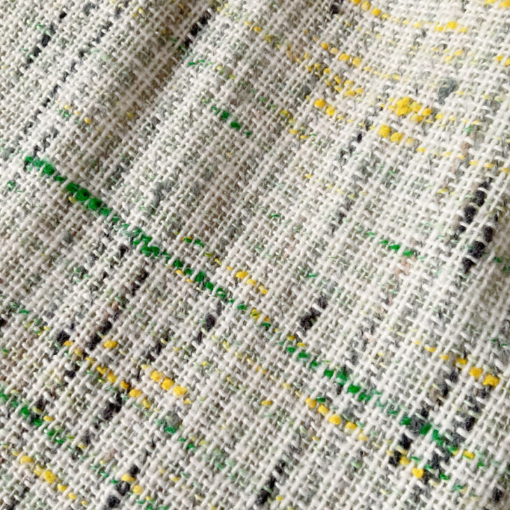 Close-up of a textured tweed-like fabric with green and yellow flecks, featured in a Chanel-inspired fashion sewing tutorial