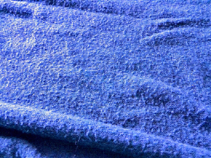 Blue sweater fabric with a rough surface, covered with lint and fabric pilling.
