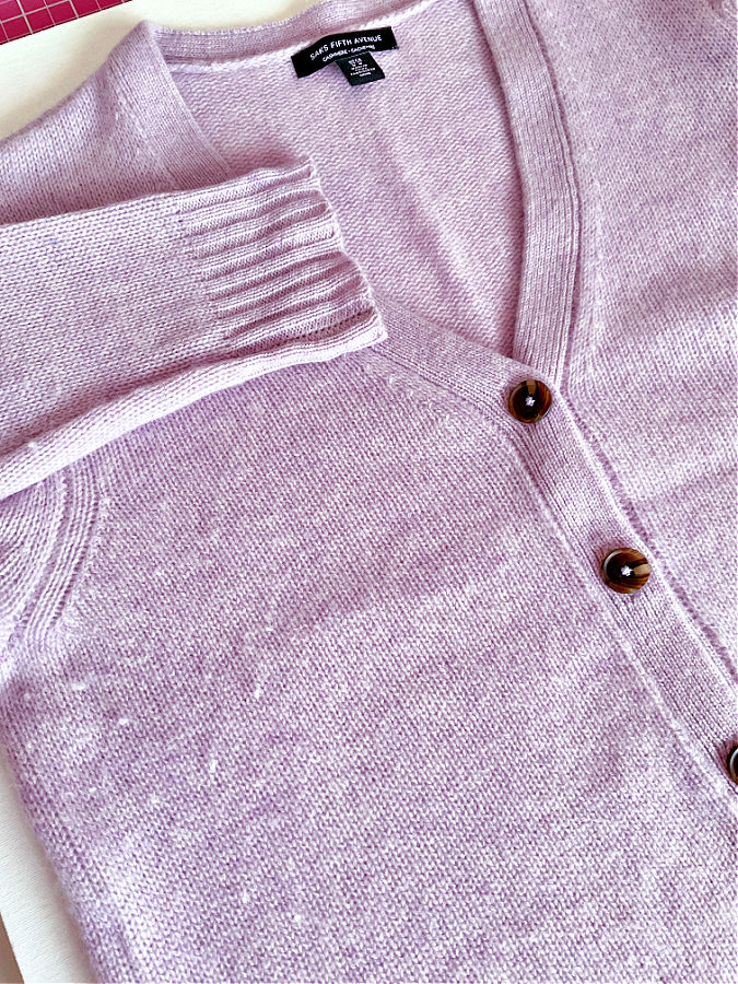 A lavender cashmere sweater with noticeable pilling and fuzz across the surface, laid flat for a close-up view.