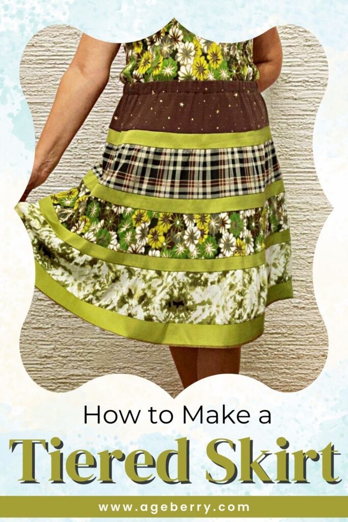 A handmade tiered skirt with multiple fabric patterns in shades of green, brown, and plaid. The skirt features gathered fabric layers separated by contrasting green trim. The person wearing the skirt is lifting the hem slightly to showcase its movement. The text overlay reads, "How to Make a Tiered Skirt," with the website ageberry.com at the bottom.