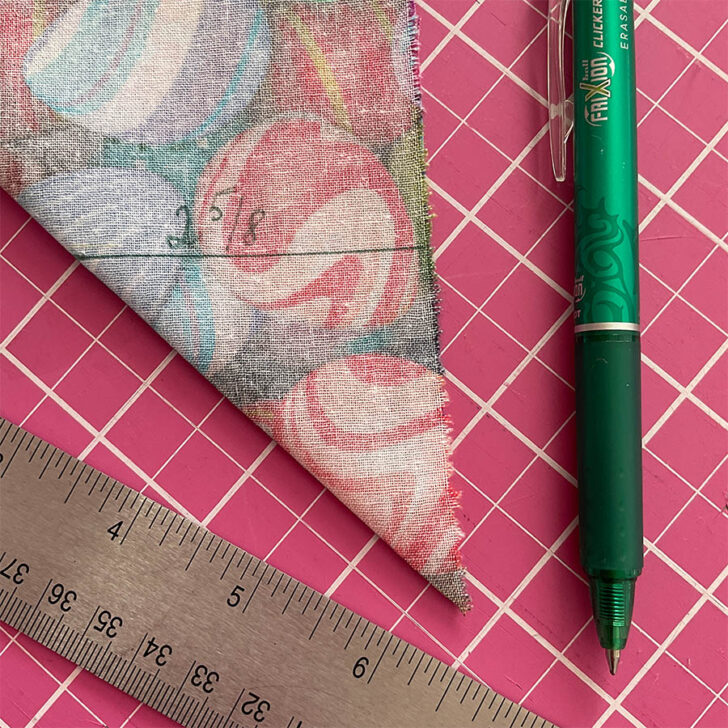 Image shows the fabric folded at the corner in preparation for sewing a mitered corner. A marking pen and a ruler are visible also.
