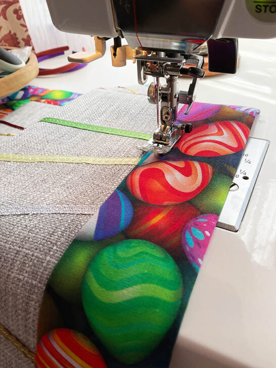 Image shows a sewing machine during the operation of final stitching of the Easter table runner on to the backing fabric using the straight stitch.