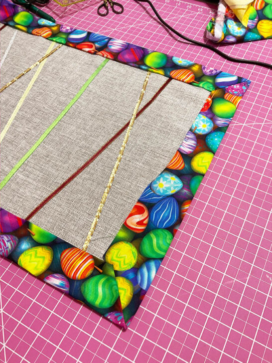 Image shows the partially folded edge of the backing fabric with magic pins inserted to secure the fold before stitching