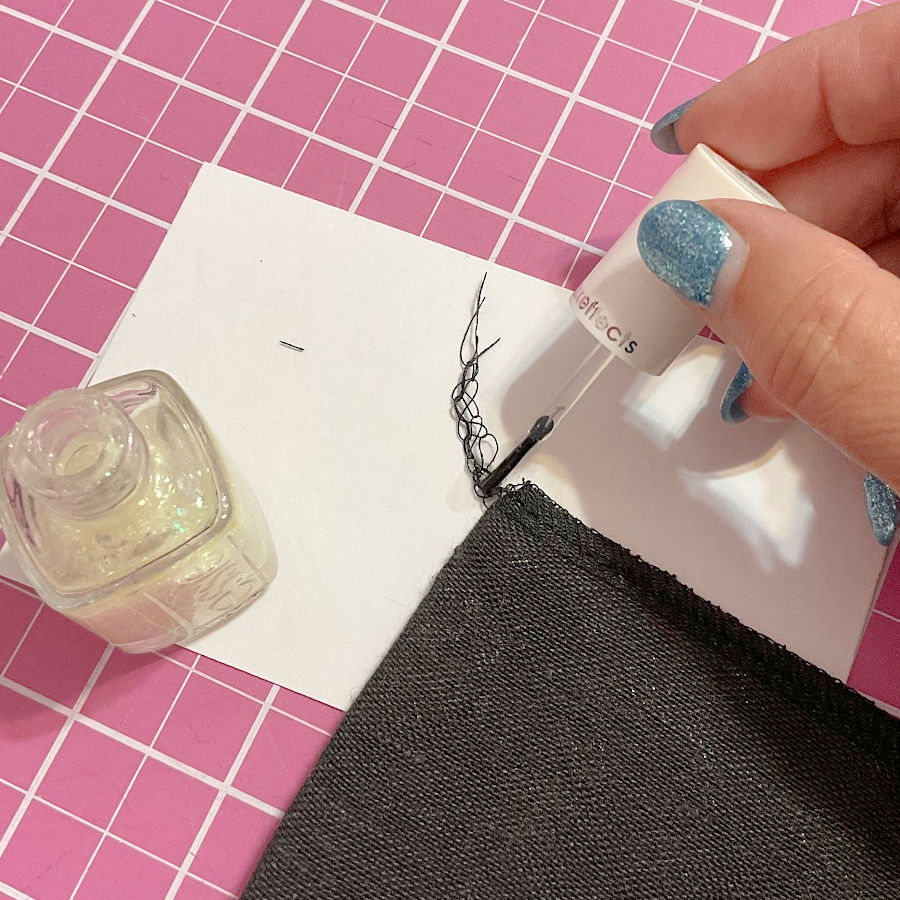 A woman's hand placing a drop of nail polish on the thread tails resulting after finishing the material edge with a serger overlock
