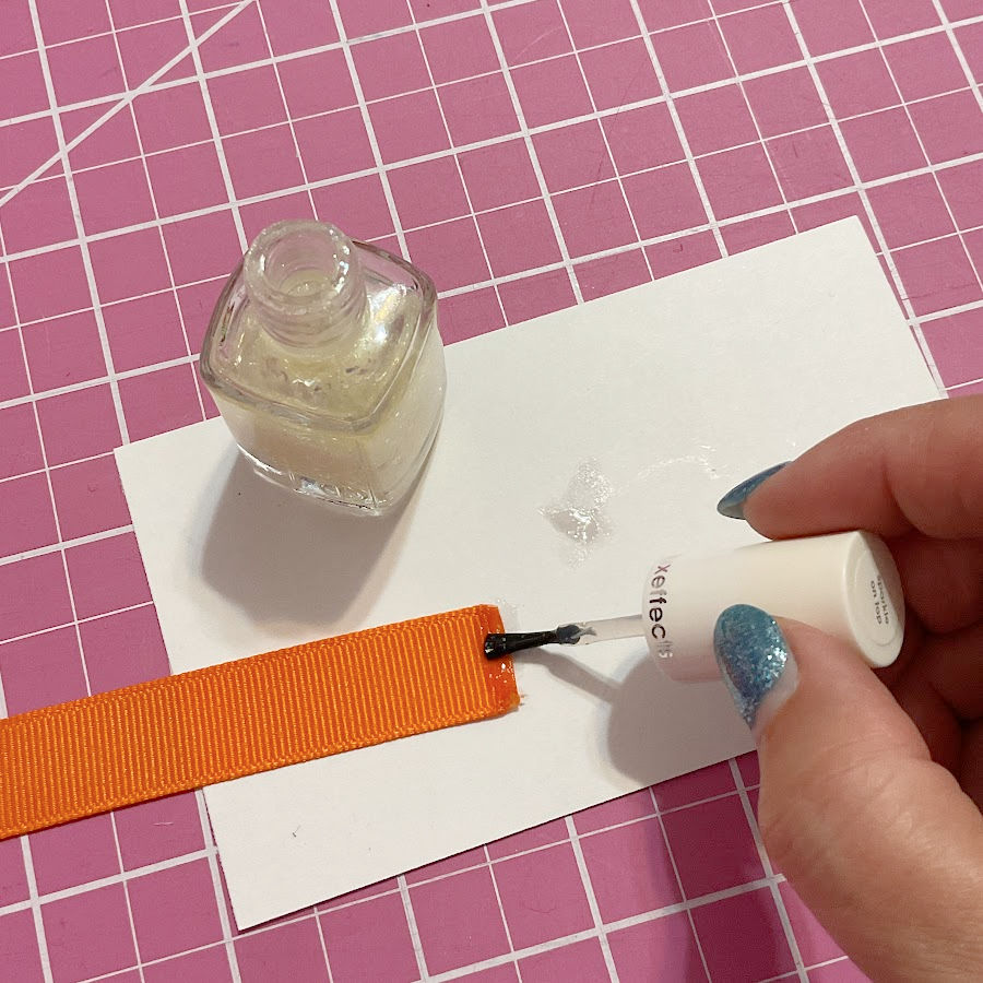 A woman's hand placing a drop of nail polish on the end of an elastic or ribbon piece after cutting