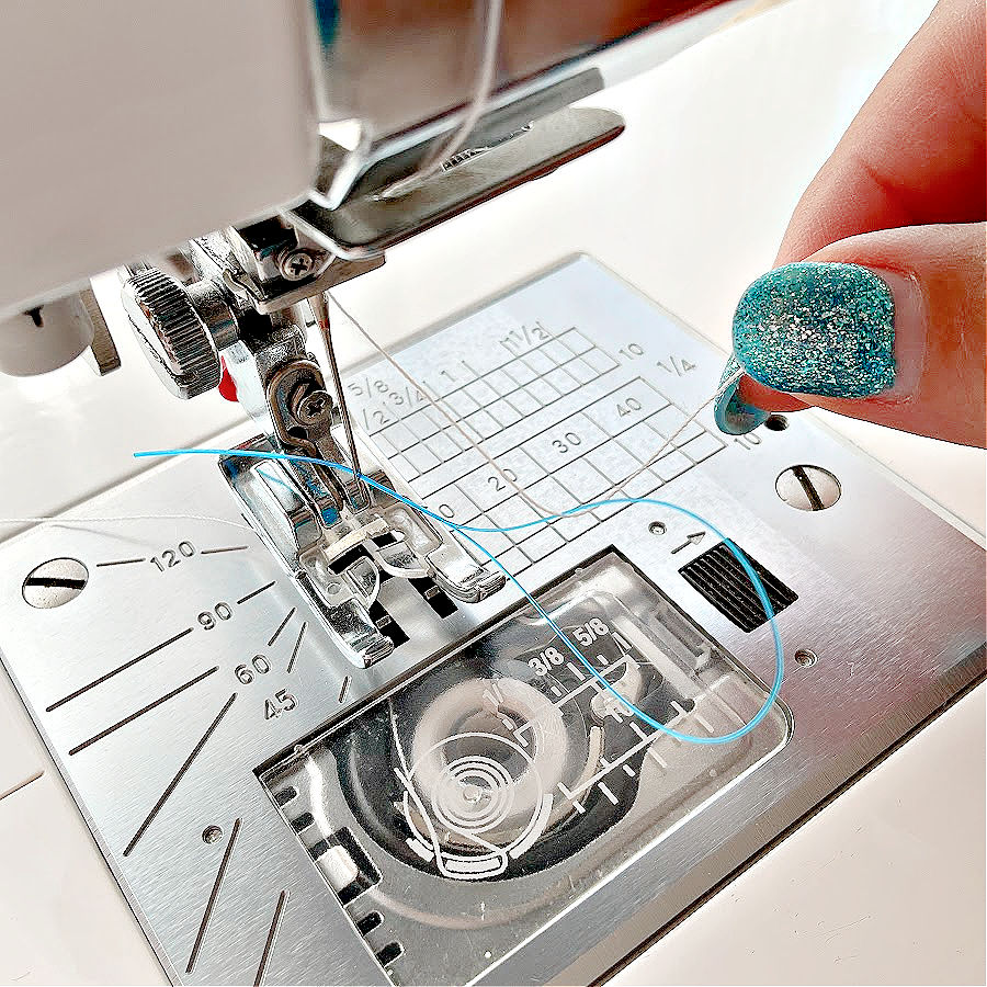 A sewing machine needle assembly in the process of being threaded using a piece of floss threader