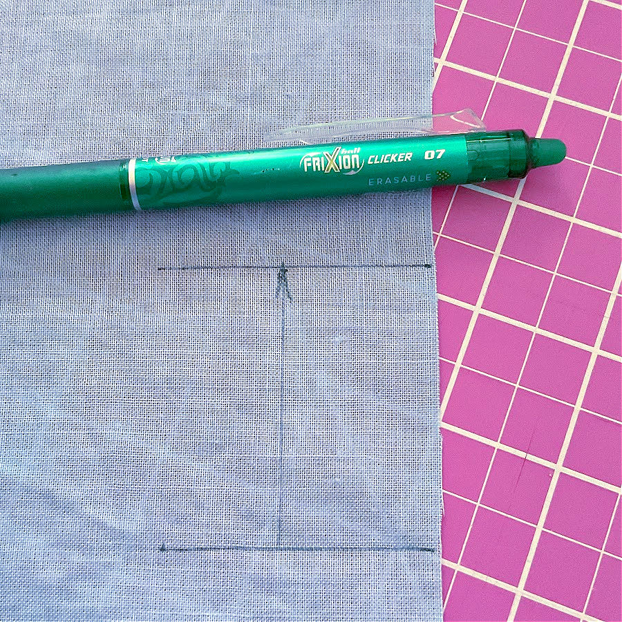 A heat erasable frixion pen on a piece of material with a mark on it. A pink cutting mat in the background.