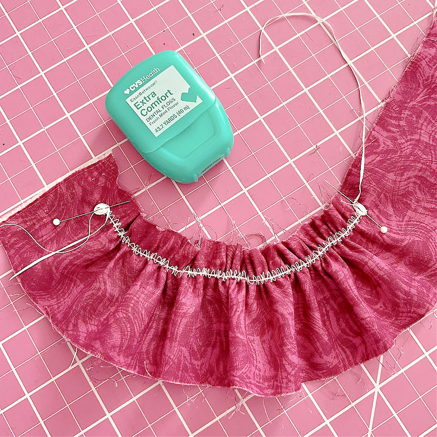 A package of dental floss on a pink cutting mat and a piece of dental floss used for gathering fabric