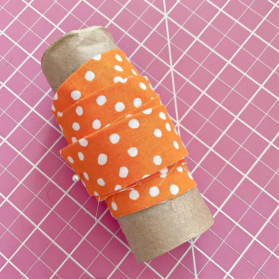 An empty toilet paper tube with bias tape wound on it for storage.