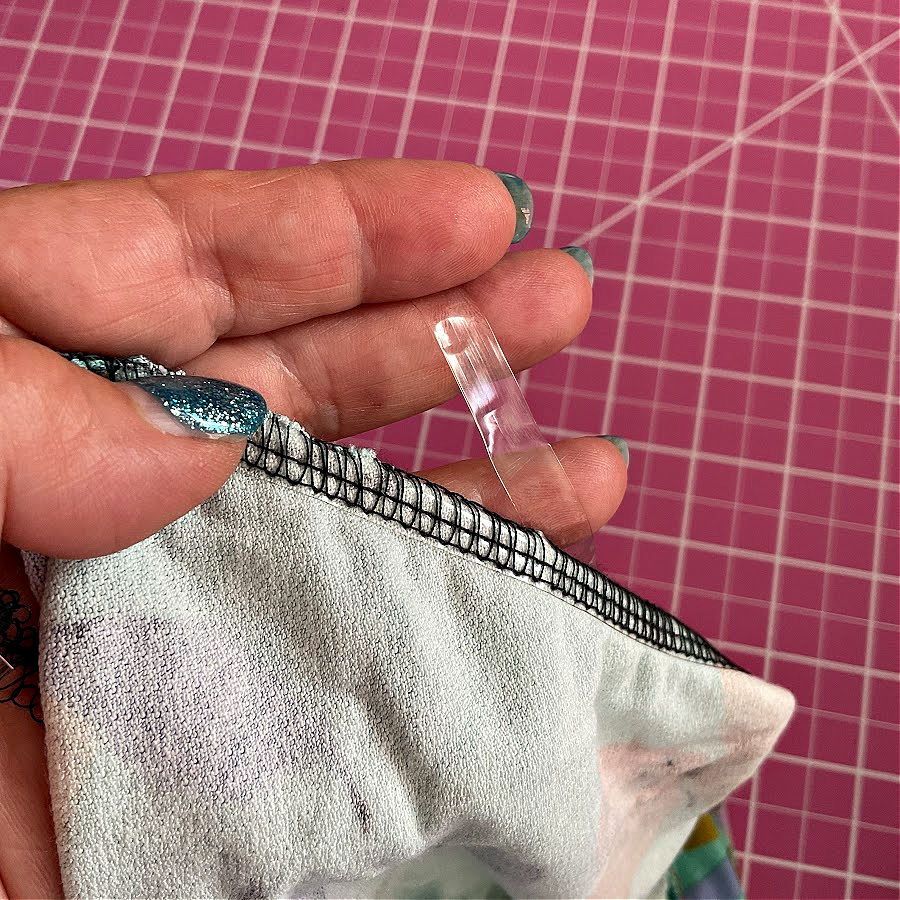 A woman's hand holding a piece of fabric and a piece of clear elastic