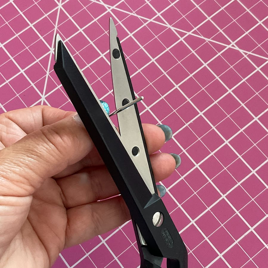A woman's hand holding a needle while simulating the cutting action with a pair of scissors with the purpose of sharpening the scissors