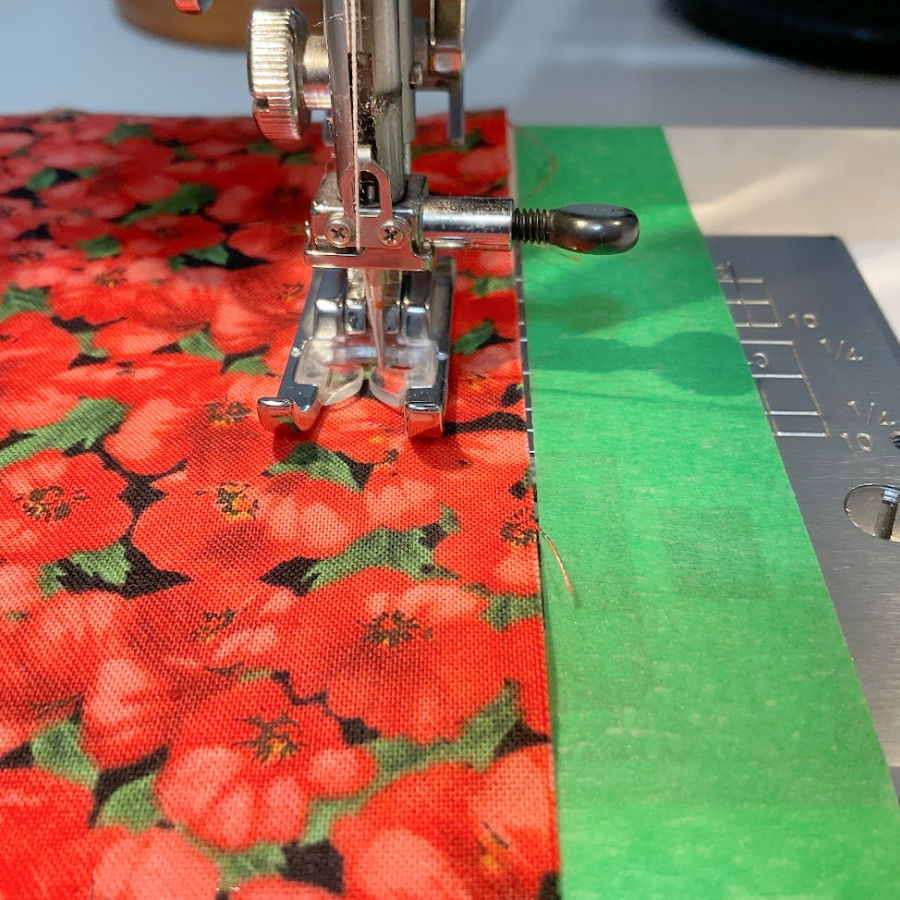 A close up of a sewing machine needle assembly and strip of painter's tape used as a seam guide.