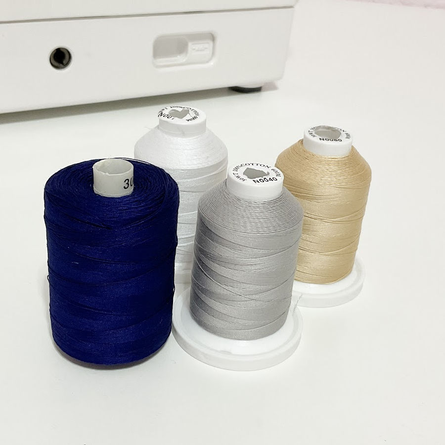 Image of four cones of thread in the most frequently used colors white, grey, beige, dark blue