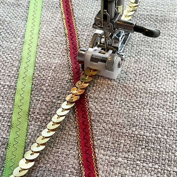 A close-up of the sequin ribbon presser foot while sewing a ribbon of sequins. The image also shows two other decorative ribbons already sewn.