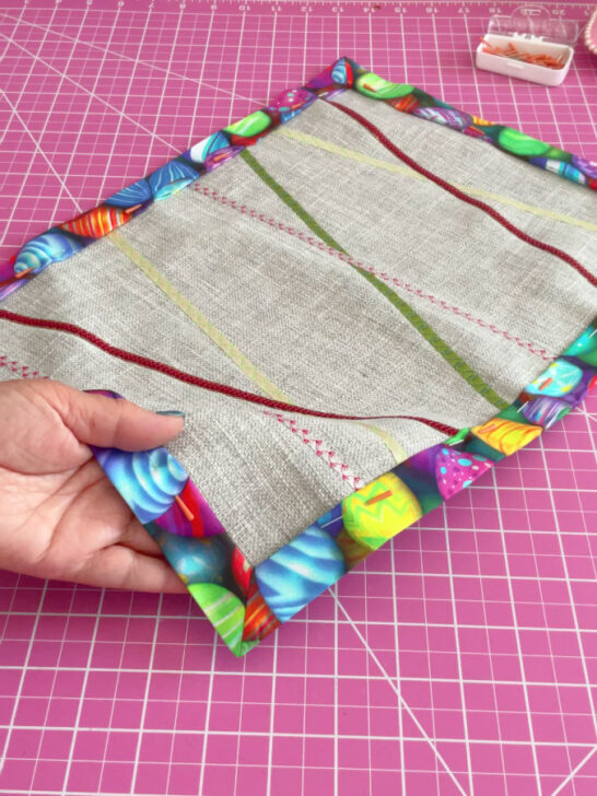 Image shows the placemat after the backing fabric was folded around and pinned with magic pins