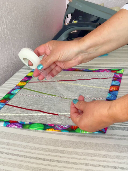 Image shows a woman's hand with a roll of hem tape. In the background the easter table runner and an iron