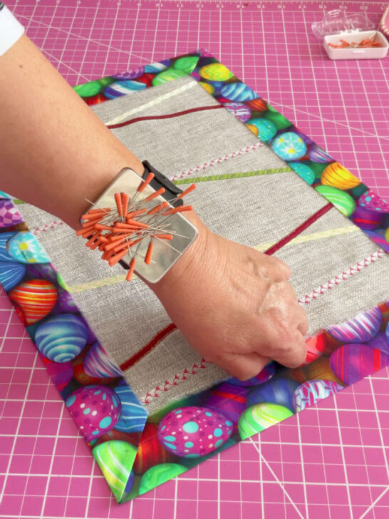 Image shows a woman's hand with a magnetic pin holder having magic pins inside while pinning the Easter placemat
