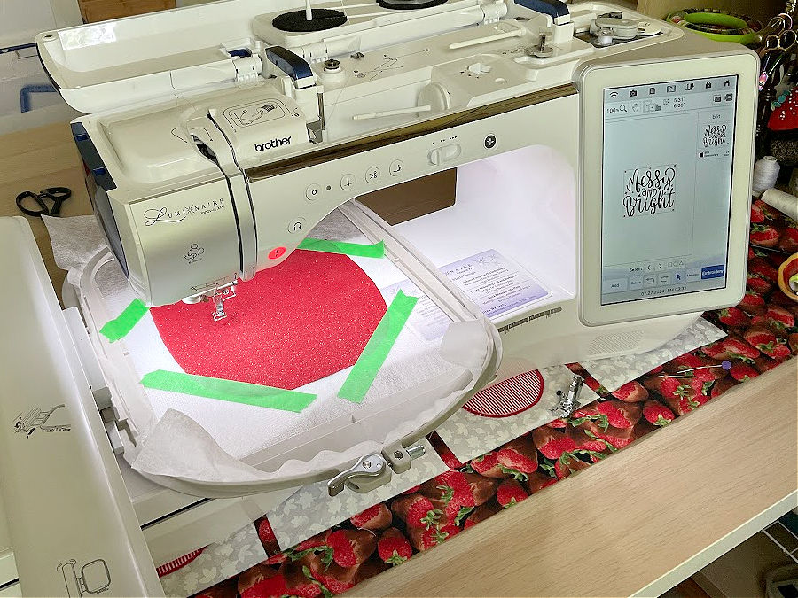A having embroidery machine with the material in the hoop having another piece of material affixed on top of this with four strips of painters tape