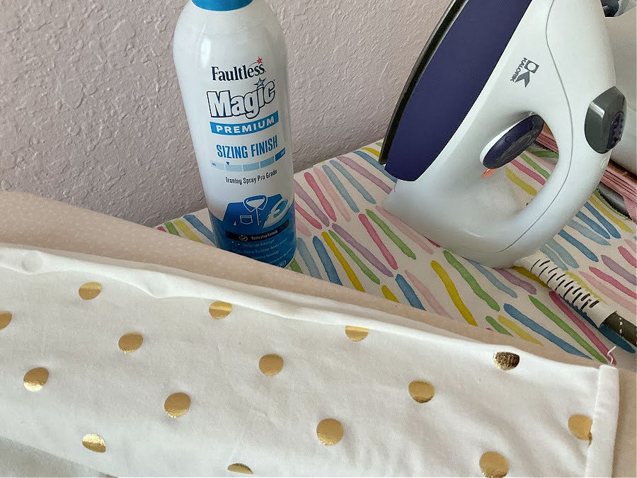 A can of Faultless magic spray for fabric on an ironing board with a steam iron visible.