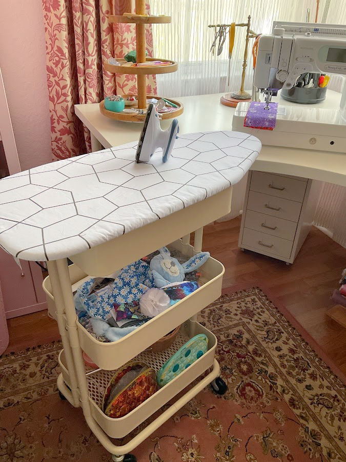 A mobile pressing station made from an Ikea cart and a mini ironing board near a sewing table with a sewing machine on it