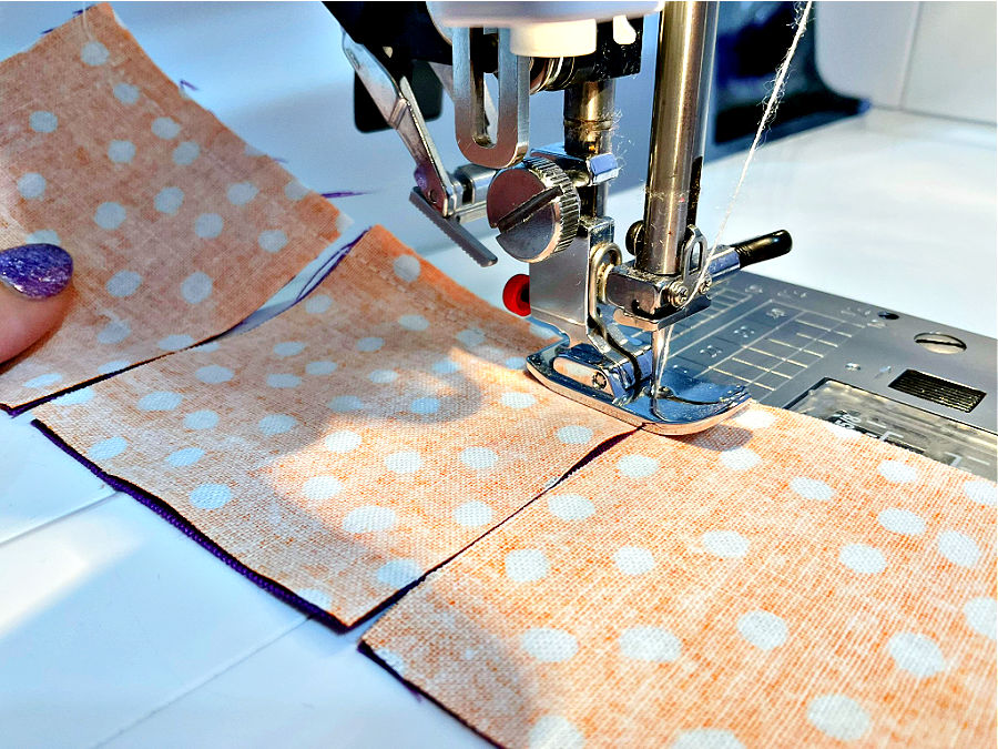 Image shows a sewing machine sewing a seam during the process of chain piecing