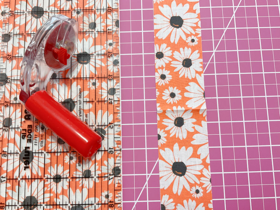 A rotary cutter sitting on a quilting ruler on top of a cutting mat. A strip of material that resulted from a recent cut is also in the image
