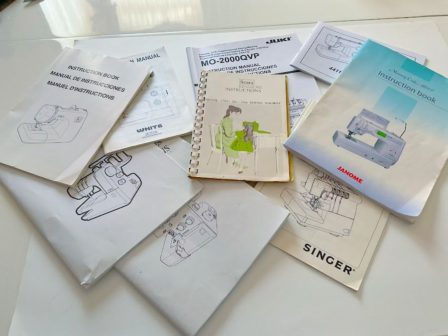 Various sewing machine manuals Janome Singer Sears White Juki spread on a sewing table