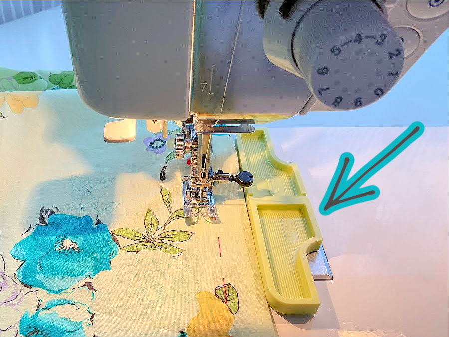 A seam guide shown mounted on a sewing machine while sewing a straight stitch