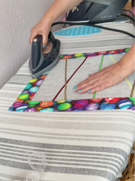 A woman ironing the Easter table runner to fix the wonder tape before final stitching