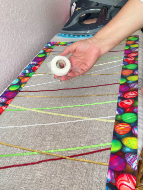 Image shows a woman's hand with a roll of wonder tape. In the background the easter table runner and an iron