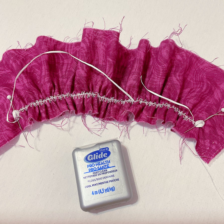 A small container of dental floss and a pink fabric gathered using dental floss as thread.